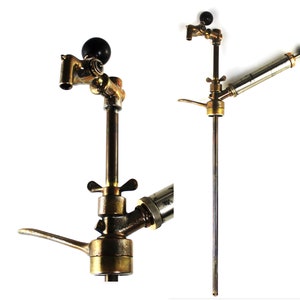 May include: An antique brass beer tap with a black knob and lever. The tap has a long, slender body with a detailed design. The image shows the tap from multiple angles, highlighting its vintage aesthetic.