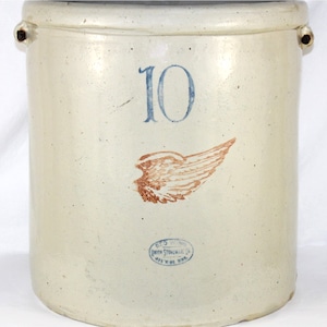 May include: A vintage stoneware crock with a cream-colored glaze. The number "10" is painted in blue, and a brown and orange wing emblem is below it. The crock has two small handles and a blue stamp that reads "RED WING UNION STONEWARE CO. RED WING, MINN. U.S.A."