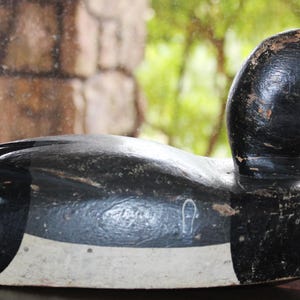 May include: A black and white wooden duck decoy with a white band around the middle. The decoy has a black head and a long, thin beak.