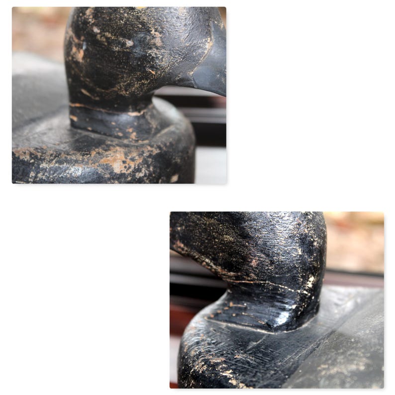 May include: Close-up of a black wooden duck decoy with a weathered finish. The decoy has a detailed head and neck, and the paint is chipped in places.