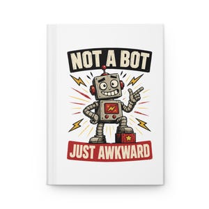 May include: A white hardcover notebook featuring a graphic of a grey robot with a red lightning bolt on its chest. The text above reads NOT A BOT and the text below reads JUST AWKWARD, with yellow lightning bolt accents surrounding the robot figure.
