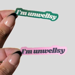 以下が含まれることがあります： 太字の丸みを帯びたフォントで「I'm unwellsy」というテキストが書かれた、ダイカットビニールステッカー2枚。上のステッカーは濃い緑色の背景に白い文字、下のステッカーは薄いピンク色の背景に濃い灰色の文字がデザインされています。