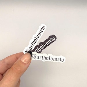 May include: Three die-cut stickers featuring the name Bartholomew written in a black gothic-style font. Two stickers have white backgrounds with black text, while the middle sticker has a black background with white text, all arranged in a fan shape.