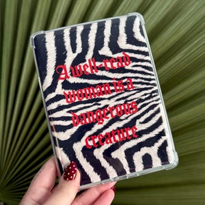Op de afbeelding: Een rechthoekige transparante beschermhoes voor een elektronisch apparaat met een zwart-wit zebrapatroon. De tekst A well-read woman is a dangerous creature is in een vetgedrukt rood gotisch lettertype in het midden van de hoes gedrukt.