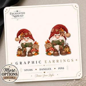 May include: A display card for Enchanted Nomad Designs featuring two gnome illustrations with red hats, green sweaters, and brown boots. The gnomes stand next to lanterns and mushrooms with signs reading Grumpy but Cute. Text includes Graphic Earrings, Studs, Dangles, Pins.