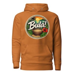 Può includere: Una felpa con cappuccio color senape con una grafica circolare sul petto. Il disegno mostra un tramonto tropicale, una ciotola, foglie verdi, un fiore di ibisco rosso e la parola Bula! in bianco. La felpa include un cappuccio e una tasca.