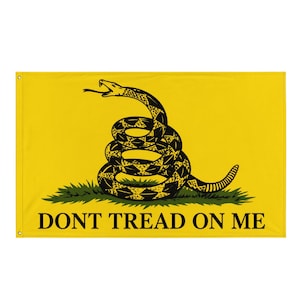 Könnte beinhalten: Eine rechteckige gelbe Flagge mit einer zusammengerollten schwarzen Klapperschlange auf einem grünen Grasbüschel. Der Text DONT TREAD ON ME ist in schwarzen Großbuchstaben im unteren Teil der Flagge gedruckt, die mit Metallösen versehen ist.