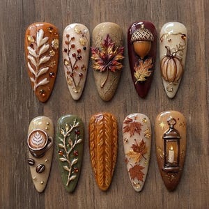 May include: A set of ten almond-shaped press-on nails featuring 3D autumn-themed designs including a white leaf, berry branches, a maple leaf, an acorn, a pumpkin, a coffee cup, a knit sweater texture, fallen leaves, and a lit lantern.