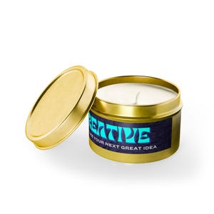 Könnte beinhalten: Eine goldfarbene Kerzendose aus Metall mit einem passenden Deckel auf der linken Seite. Der Behälter hat ein dunkles Etikett mit dem hellblauen Text CREATIVE und dem weißen Text LIKE YOUR NEXT GREAT IDEA. Die Kerze im Inneren ist weiß.