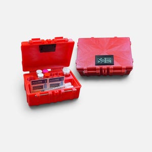 Op de afbeelding: Een felrode, rechthoekige opbergkoffer met een scharnierend deksel en een digitaal hygrometerdisplay aan de buitenkant. De open koffer toont interne compartimenten met kleine witte bakjes en twee zakjes met het label Alcohol SWAB.