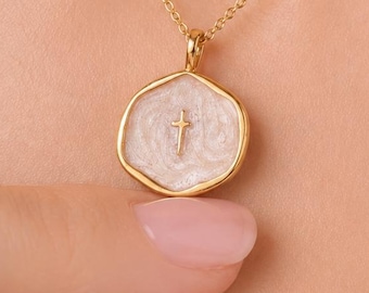 Puede incluir: Un collar de cadena dorada con un colgante hexagonal que presenta una incrustación de esmalte nacarado en color blanco roto. En el centro de la superficie esmaltada hay una pequeña cruz dorada en relieve. El colgante tiene un borde dorado pulido.
