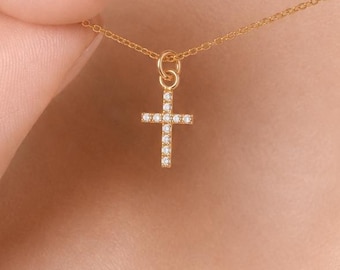 Puede incluir: Un collar de cadena dorada fina con un pequeño colgante de cruz. La cruz está adornada con una serie de diminutas piedras claras y brillantes engastadas a lo largo de sus barras verticales y horizontales, suspendida de una argolla circular.