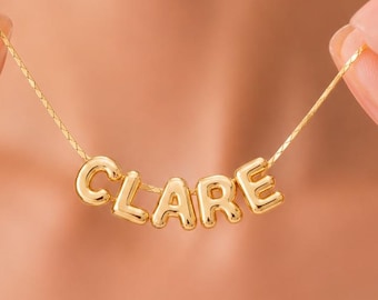 Puede incluir: Un collar de tono dorado con cinco dijes de letras metálicas, redondeadas e individuales, que forman el nombre CLARE. Las letras están ensartadas en una cadena fina y delicada de color dorado, creando una pieza de joyería personalizada.