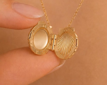 Puede incluir: Un collar con colgante de relicario en metal dorado que presenta una cadena fina y un dije circular que se abre mediante una bisagra. El interior del relicario muestra una superficie lisa y plana en un lado y un patrón de concha radiante en el otro.