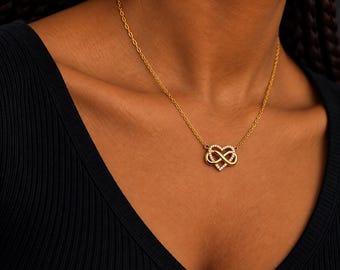 Puede incluir: Un collar de tono dorado con un colgante que combina una forma de corazón con un símbolo de infinito. El colgante está adornado con pequeñas piedras transparentes a lo largo del contorno del corazón. La cadena es fina y dorada.
