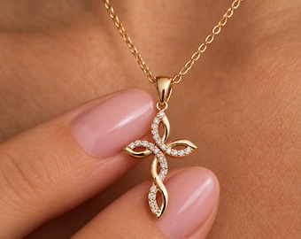 Puede incluir: Un collar de tono dorado con un colgante de cruz con un diseño entrelazado de estilo infinito. El colgante está adornado con pequeñas piedras claras y brillantes engastadas a lo largo del marco de metal curvo.