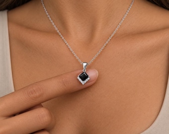 Puede incluir: Un collar de plata con un colgante de piedra negra de corte cuadrado. El colgante está adornado con pequeñas piedras claras de corte redondo a lo largo de los dos bordes inferiores, suspendido de una fina cadena de plata.