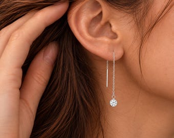 Puede incluir: Un pendiente de hilo de plata con una cadena fina que atraviesa el lóbulo de la oreja y termina en una pequeña piedra redonda engastada. El pendiente incluye una barra de plata fina y recta en el otro extremo de la cadena.