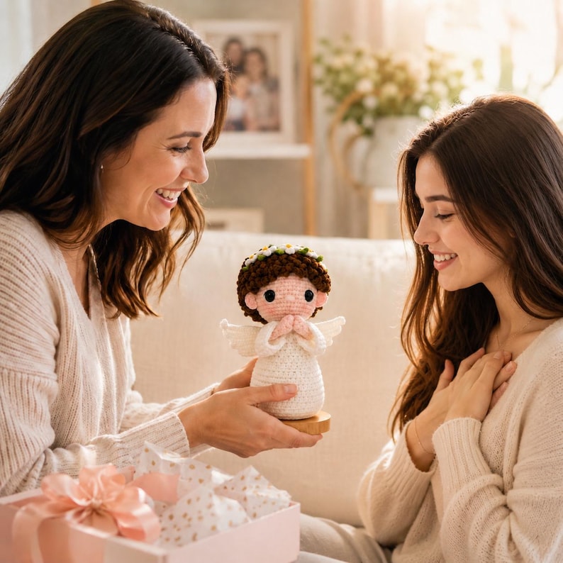 May include: A small crocheted angel figurine with brown hair, a white dress, and a crown of tiny white flowers. The angel has pink cheeks, black eyes, and hands pressed together in a prayer position, mounted on a circular wooden base.