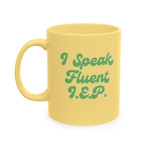 May include: A pale yellow ceramic mug featuring a curved handle and the green text "I Speak Fluent I.E.P." printed in a bold, rounded font on the front. The mug has a smooth, solid-colored exterior and a standard cylindrical shape for beverages.