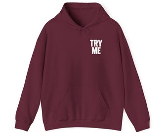 May include: A deep burgundy hooded sweatshirt featuring long sleeves, a front kangaroo pocket, and the text TRY ME printed in white on the upper left chest area. The garment includes a matching drawstring hood and ribbed cuffs and hem.