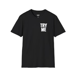May include: A black short-sleeve t-shirt featuring a crew neckline and the text TRY ME printed in bold white capital letters on the upper left chest area. The garment has a standard fit with a straight hemline and a visible interior neck label.