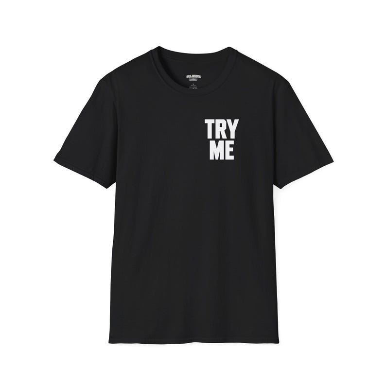 May include: A black short-sleeve t-shirt featuring a crew neckline and the text TRY ME printed in bold white capital letters on the upper left chest area. The garment has a standard fit with a straight hemline and a visible interior neck label.