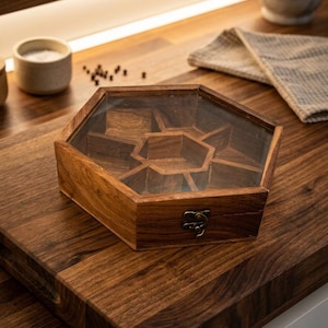 May include: A hexagonal wooden storage box with a clear glass lid and a metal latch. The interior is divided into seven separate compartments, featuring a central hexagonal section surrounded by six triangular-shaped storage spaces.
