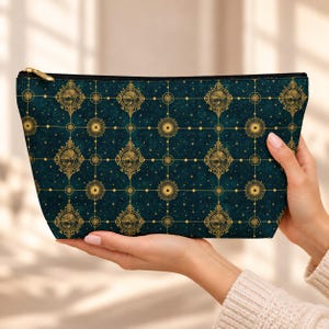 Può includere: Una pochette con cerniera color verde ottanio scuro caratterizzata da un motivo dorato ripetuto di mappe celesti circolari, cornici geometriche complesse e piccole stelle a quattro punte su uno sfondo testurizzato.