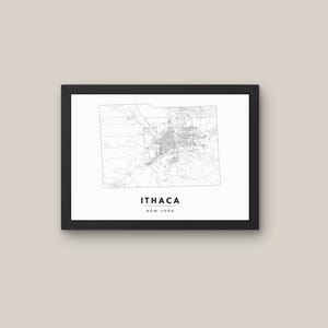 May include: A framed wall art print featuring a black and white map of Ithaca, New York. The map displays intricate street grids and geographic boundaries on a white background. Below the map, the text reads ITHACA NEW YORK in black capital letters.