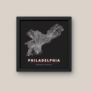 Può includere: Un'opera d'arte da parete quadrata incorniciata che presenta una dettagliata mappa stradale bianca di Philadelphia, Pennsylvania, su uno sfondo nero solido. La mappa è delineata da una sottile linea rossa, con il testo PHILADELPHIA PENNSYLVANIA stampato sotto.