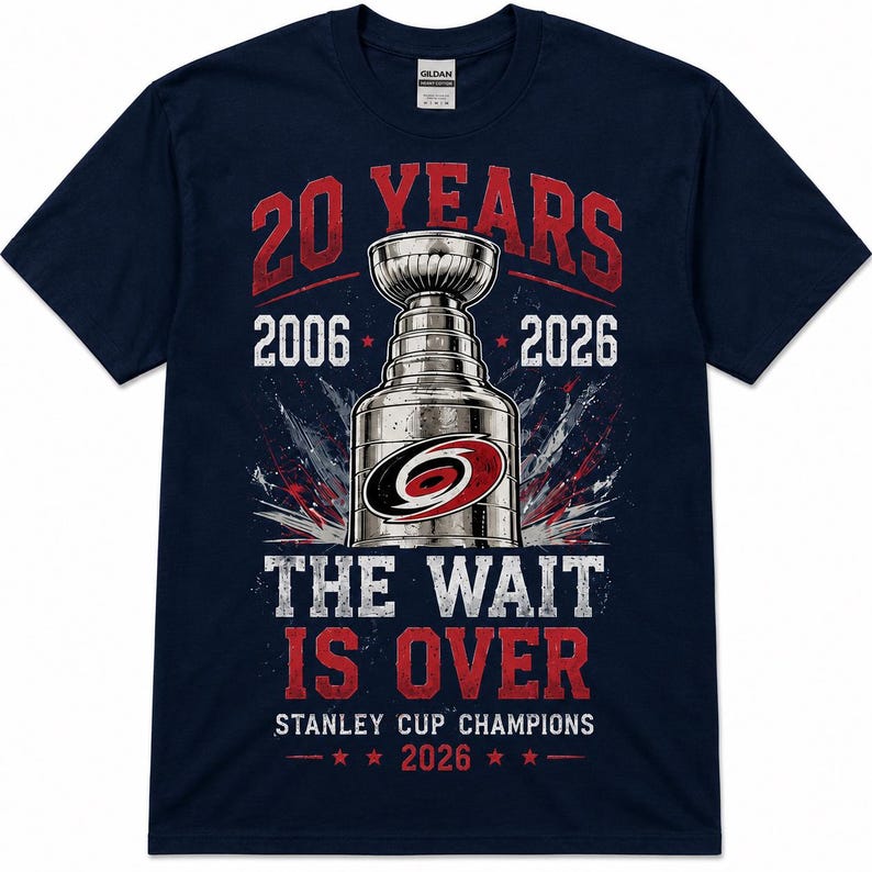 May include: A navy blue short-sleeve t-shirt featuring a graphic of a silver trophy cup with a red and black logo. Text reads 20 YEARS, 2006, 2026, THE WAIT IS OVER, STANLEY CUP CHAMPIONS, and 2026, accented with red stars and a distressed design.