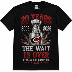 May include: A black short-sleeve t-shirt featuring a graphic of the Stanley Cup trophy in the center. Text reads 20 YEARS, 2006, 2026, THE WAIT IS OVER, and STANLEY CUP CHAMPIONS 2026. The design includes red and white accents and a team logo.