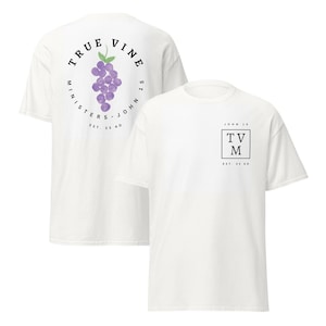 May include: A white short-sleeve t-shirt featuring a front chest graphic with a black square containing the letters TVM, the text JOHN 15, and EST. 33 AD. The back displays a circular design with a purple grape cluster and TRUE VINE MINISTERS.