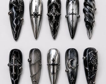 May include: A set of ten stiletto-shaped press-on nails featuring a black, silver, and grey color palette. The designs include metallic cross emblems, silver chains, a crescent moon, a rose, and swirling patterns with small silver spherical studs.