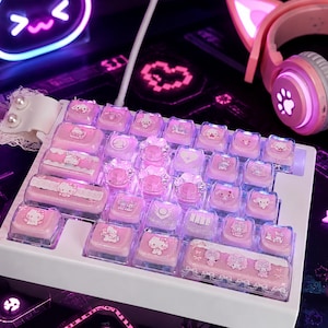 Peut inclure: Un clavier mécanique blanc doté de touches roses personnalisées avec diverses illustrations de personnages Sanrio, dont Hello Kitty et My Melody. Les touches ont une finition translucide et le clavier est orné d'un nœud en dentelle blanche.