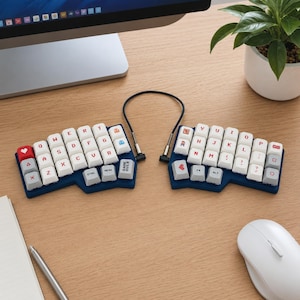 Puede incluir: Un teclado mecánico ergonómico dividido en dos mitades de color azul oscuro conectadas por un cable negro. Las teclas blancas tienen letras rojas y varios iconos pequeños de colores, incluyendo un corazón, un fantasma y un personaje pixelado, con teclas grises.