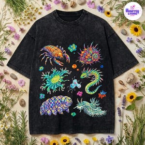 May include: A black acid-wash t-shirt featuring a vibrant, multi-colored graphic print of various microscopic organisms and sea creatures, including a tardigrade, a sea slug, and a crustacean, arranged in a scattered pattern across the front.