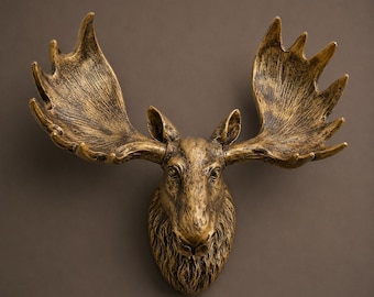 Può includere: Una scultura da parete raffigurante una testa di alce con finitura oro metallizzato e dettagli marrone scuro anticato. L'oggetto presenta un volto dettagliato con pelo testurizzato e grandi palchi ramificati che si estendono verso l'esterno.