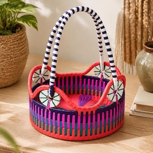 May include: A round woven basket featuring a vibrant color palette of hot pink, deep purple, and teal vertical strips. The basket includes a scalloped top edge and a tall, arched handle with a white and navy blue striped pattern.