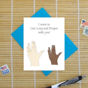 May include: A greeting card with a blue envelope. The card features a hand drawn illustration of two hands making the Vulcan salute, with wedding rings on their ring fingers. The text on the card reads "I want to Live Long and Prosper with you!"