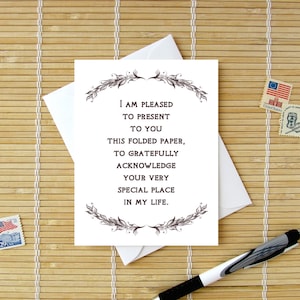 May include: A white card with a black border and black text that reads "I am pleased to present to you this folded paper, to gratefully acknowledge your very special place in my life." The card is decorated with a black floral design.