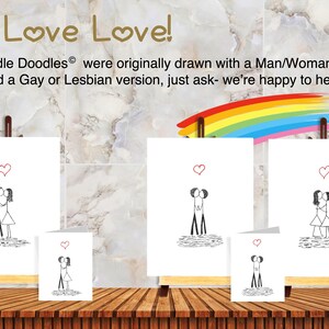 May include: Three white greeting cards and three matching prints on wooden easels, each featuring a black ink stick figure couple kissing under a red heart. The text reads: We Love Love! All Canoodle Doodles were originally drawn with a couple.