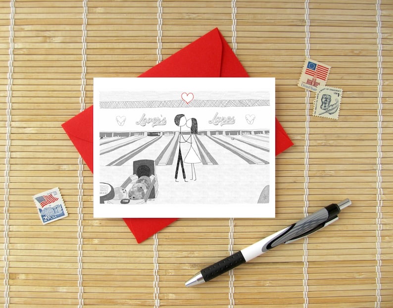 May include: A white greeting card featuring a black and white line drawing of two stick figures kissing at a bowling alley. The text "Lover's Lanes" is written above the bowling lanes, with a red heart drawn above the figures and two smaller hearts on the sides.