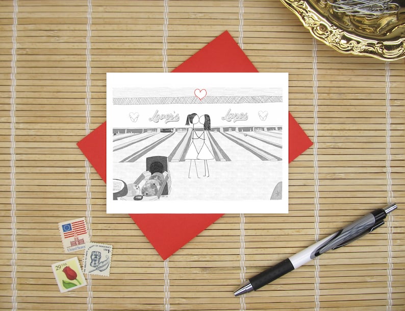 May include: A white greeting card featuring a black and white line drawing of two stick figures kissing at a bowling alley. The text "Lover's Lanes" is written above the figures, with a small red heart centered above the text.