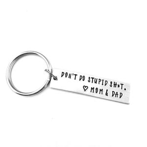 May include: A silver-colored keychain with a rectangular tag. The tag has the text "DON'T DO STUPID SH*T. ❤ MOM & DAD" in black, stamped lettering. The keychain ring is circular and attached to the tag.