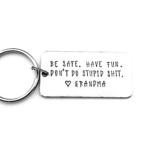 May include: A rectangular silver-toned metal keychain tag featuring the stamped black text: BE SAFE. HAVE FUN. DON'T DO STUPID SHIT. ♡ GRANDMA. The tag is attached to a circular metal split ring, presenting a clean, metallic finish throughout.