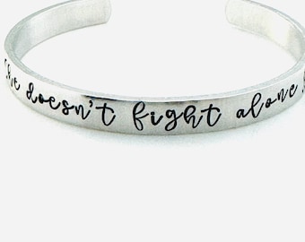 She doesn't fight alone: Hand Stamped Aluminum Bracelet with Cancer Awareness Ribbon