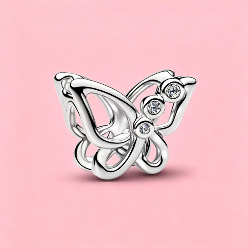 May include: A silver-toned butterfly charm featuring an openwork design with smooth, polished edges. The upper wing section is accented with three small, clear, round-cut stones set in a vertical row along the inner edge of the metal frame.