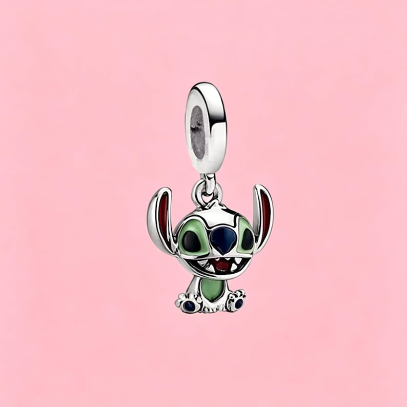 May include: A silver charm featuring the character Stitch with light green enamel on the ears and chest, dark blue enamel on the nose and eyes, and a red mouth. The charm has a polished silver finish and a circular bail for attachment to a bracelet.